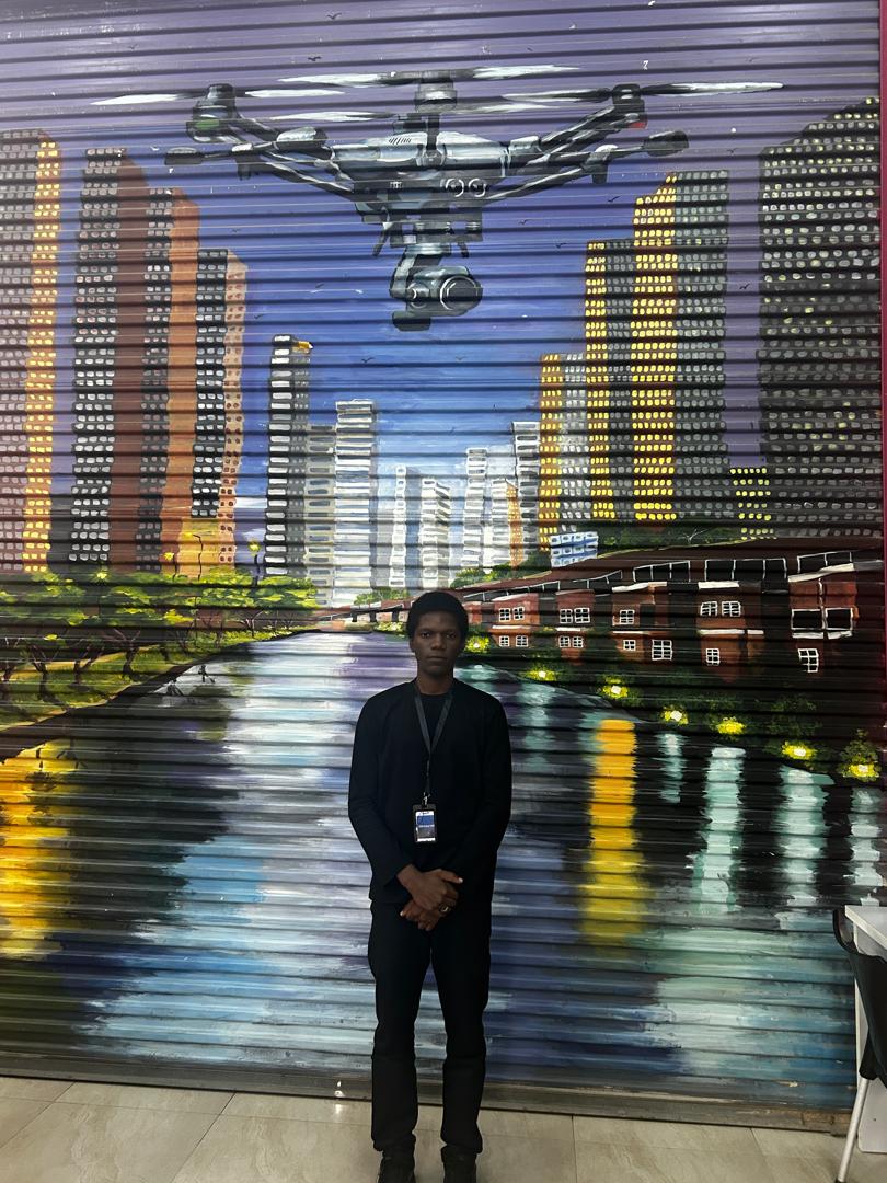 Dave Olaniyan standing in front of a city and drone mural